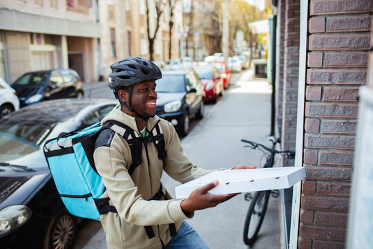 Happy delivery man with a pizza box on a city street