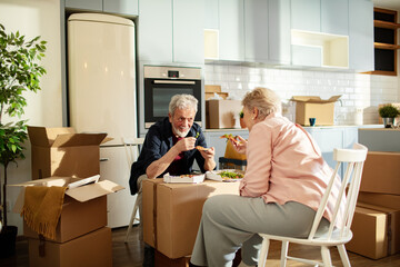Senior couple eating pizza on moving boxes at home