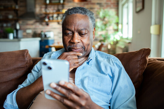 Senior black man using smartphone on the couch - Powered by Adobe