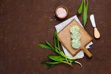 Cooked butter with wild garlic, parsley and salt on a wooden board on a brown concrete background....