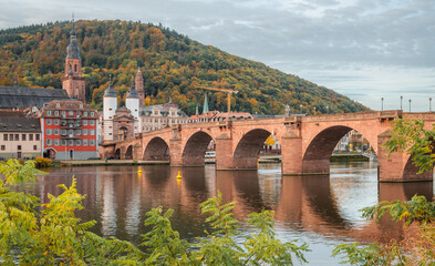 View on the Karl Theodor Bridge (German: Karl-Theodor-Brücke) and the old gate in the german city Heidelberg during early morning on a cloudy day. Heidelberg on Neckar river. - obrazy, fototapety, plakaty
