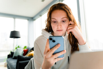 A woman uses a mobile phone and laptop at home