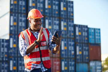 African factory worker or engineer holding tablet and video call to someone in containers warehouse...
