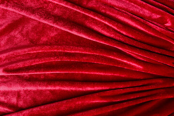 Textured background of deep red velvet fabric with folds.