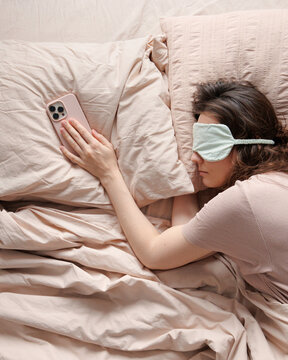 Top view of person sleeps in mask with phone in hand.