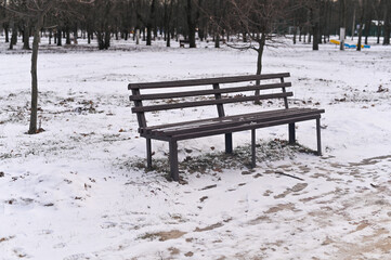 an empty park bench. Snow on the ground