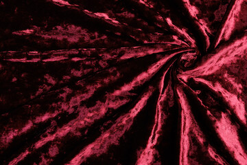 Textured background of deep red velour fabric with folds.