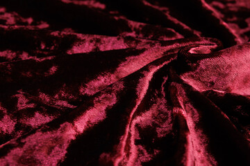 Textured background of deep red velour fabric with folds.