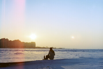 a girl drinks tea from a thermos and admires the winter sunset
