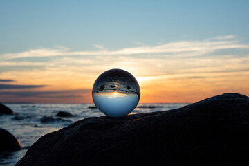 Ball made of glass lies on a stone in which the beach and the sea are reflected - 783301373