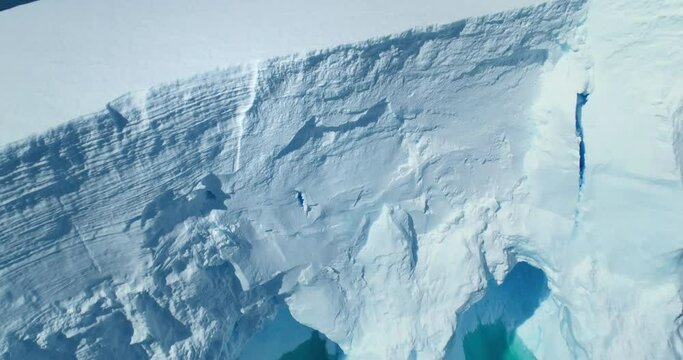 Giant ice wall melting in arctic water aerial shot. Antarctica iceberg floating turquoise water top down view. Huge glacier ice cave melting in the ocean close up. Global warming and climate change.