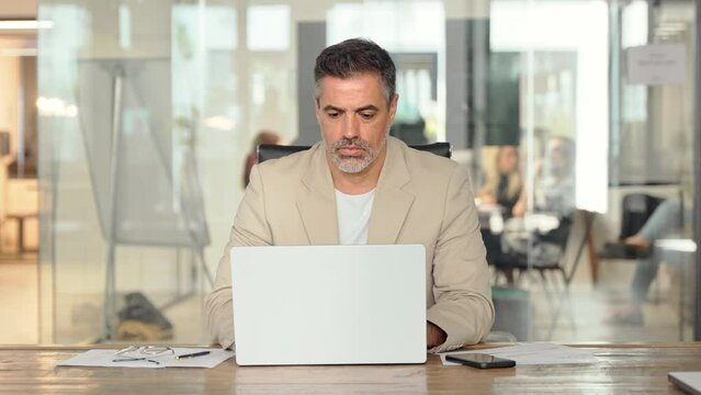 Busy mature professional business man ceo looking at laptop working at desk. Serious middle aged executive manager investor using computer thinking on digital financial investing risks in office.