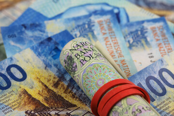 A roll of Polish banknotes lies on the flat Swiss franc banknotes, CHF, PLN