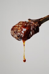 A perfectly grilled lamb chop with a glistening exterior is suspended in mid-air against a vibrant orange background. A single droplet of juice is caught in the act of falling from the meat_