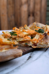 American food. Delicious pizza. Closeup view of a sliced cheddar and mozzarella cheese, french fries, green onion, tomato sauce and bacon pizza, on the white marble table with a wooden background.	
