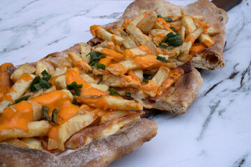 American food. Delicious pizza. Closeup view of a sliced cheddar and mozzarella cheese, french fries, green onion, tomato sauce and bacon pizza, on the white marble table