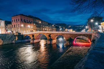 Sarajevo's old town at dusk, where the iconic Latin Bridge and traditional houses along the Miljacka River create a picturesque view of the city's historical charm. - 783326186