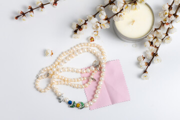 A string of pearls, a candle and blooming branches on white background