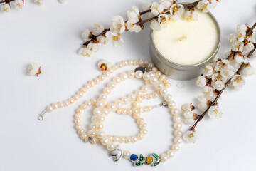 A string of pearls, a candle and blooming branches on white background