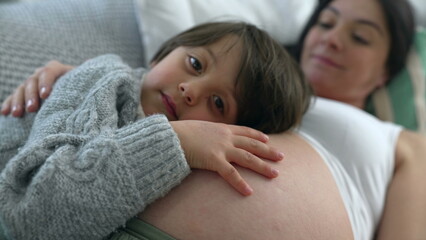 Son leaning on mother's belly during third trimester pregnancy. Tender caring relationship awaiting...