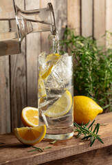 Water is poured from a decanter into a glass with ice and lemon slices.