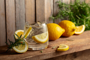 Summer refreshing drink with ice, rosemary and lemon slices on a old wooden table.