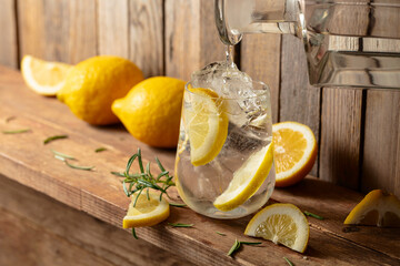Summer refreshing drink with ice, rosemary and lemon slices on a old wooden table.