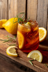 Iced tea or alcoholic cocktail with ice, rosemary and lemon slices on a old wooden table.