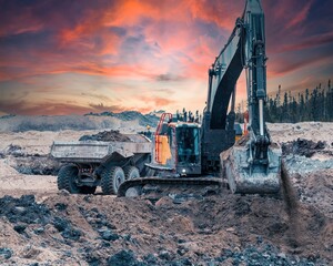 Excavator digging soil on a site at sunset, with a dump truck passing in the background