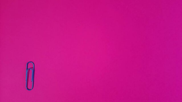 Blue paper clip rotates on pink background. Stop motion. Mockup for Copy space, text, advertising. Concept of downloading, software update, waiting. Looped video.