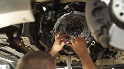 Mechanic installs clutch kit in car. Professional replaces release bearing, cover, disk on vehicle. Auto repair shop scene, hands-on maintenance.