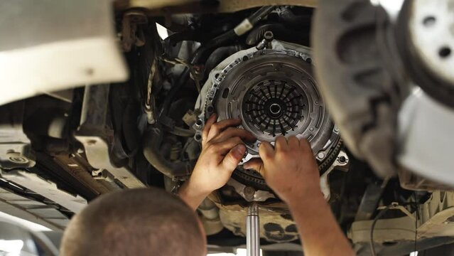 Mechanic installs clutch kit in car. Professional replaces release bearing, cover, disk on vehicle. Auto repair shop scene, hands-on maintenance.