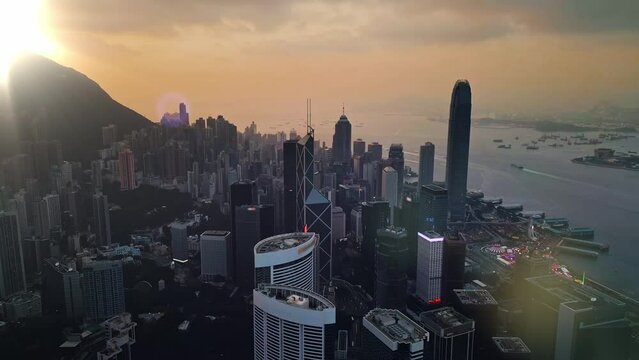 Amazing sunset over Victoria Harbor in Hong Kong city illuminating modern buildings and ships floating in the sea. Living in futuristic asian town with modern architecture on the coastline. Urban life