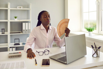 Young african american business woman employee using hand fan suffering from heat and summer high...