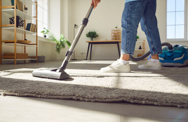 Cropped photo of woman cleaning with vacuum cleaner carpet in the living room at home. Female...