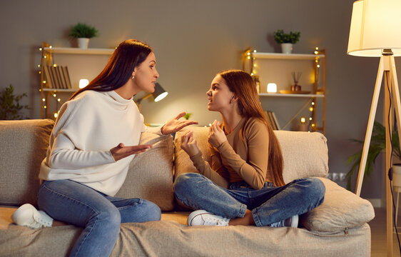 Young woman having disagreement with her teen girl daughter. Annoyed emotional mother arguing and quarreling with her child sitting on sofa at home. Family generation conflict concept.