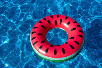 Red inflatable ring in the water of a swimming pool on a sunny day. Summer holiday concept. Inflatable ring in the shape of a watermelon