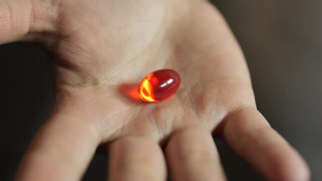 Caucasian hand opening to reveal red capsule pill tablet.