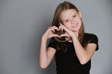 Child forms a heart with fingers, her smile adding charm. Symbolizing the purity and sincerity of young love.