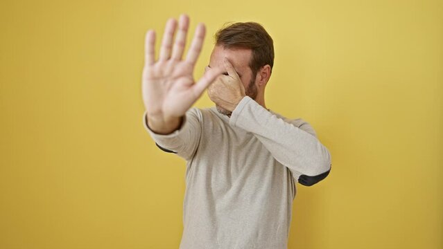 Terrified hispanic man fearfully covering eyes with hands, making stop gesture against yellow isolated background. embarrassed, showcasing negative expression- a visual portrayal of stress.
