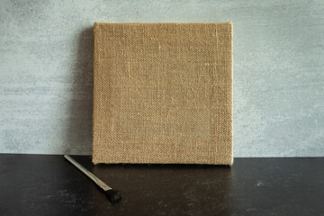 Blank brown burlap canvas against a gray background one paintbrushes laying beside it.
