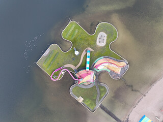 Children recreational playground, playfull colors, climbing rack, slide and other attributes on a puzzle piece on water. Aerial drone view.