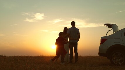 Parents children at sunset by car in field. Happy man woman hugging embracing girl boy kids running...