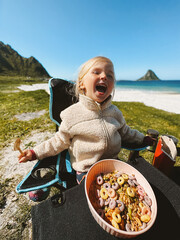 Child girl eating muesli picnic breakfast on the beach camping outdoor summer vacations travel healthy lifestyle vegan healthy food, 4 years old kid with cereal bowl candid happy emotions - 783351331