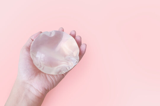 Silicone implant breast augmentation in holding on pink background, Surgery gel type and smooth touch surface in hand, medical equipment.