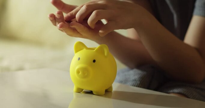 Child recounts his money and puts it in piggy bank. Schoolgirl throws coins into a yellow piggy bank. Coins in piggy bank symbol of banking security. Financial savings. Children in financial security.