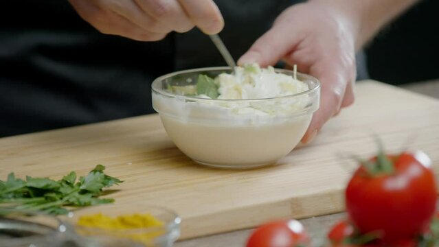 The chef mixes garlic and herbs with sour cream in a saucepan. They make a delicious white sauce, which is used in the restaurant kitchen to serve meat and fish dishes. Close up. Slow motion. 4k