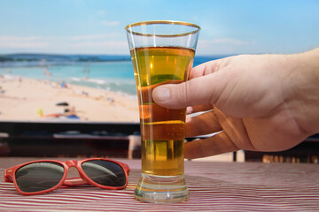 A person is holding a glass of beer with a beach scene in the background