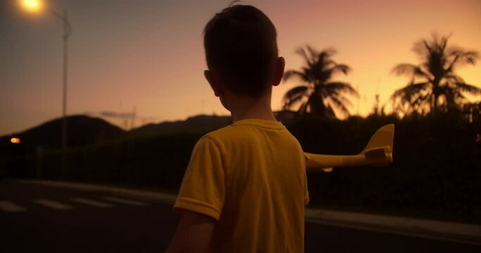 Little boy dreams of flying and becoming pilot. Child wants to become pilot and astronaut. Slow motion. Happy kid runs with a toy airplane on park in the sunset light. Children play toy airplane. 4K