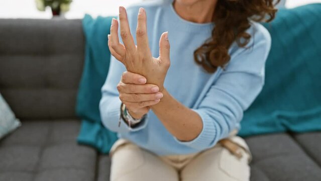 A middle-aged woman with curly hair experiences wrist pain in a home living room setting.